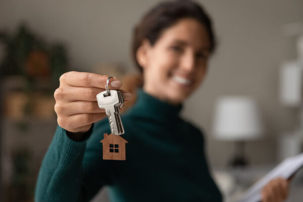 Close up focus on keys, smiling woman realtor selling apartment, offering to client, showing at camera, holding documents, contract, making purchasing deal, real estate agent, mortgage or rent